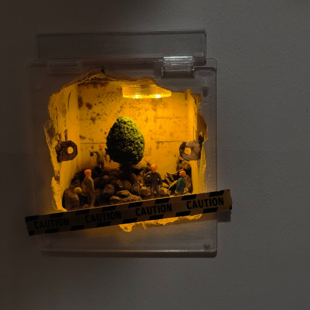 wall hole dressed as a tiny garden dig, a small tree and rocks with 1:87 workers under the yellow light