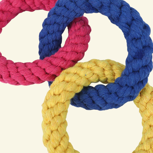 Three braided rope rings in pink, blue, and yellow, overlapping on a light cream background.