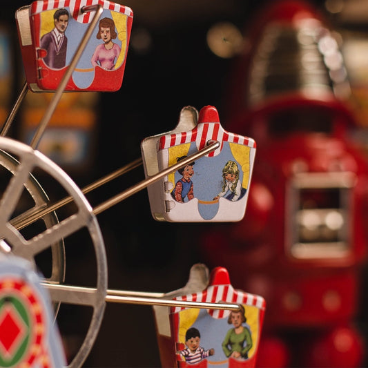 close-up of the printed tin gondolas, each with painted riders inside, hanging off the wire spokes of the ferris wheel