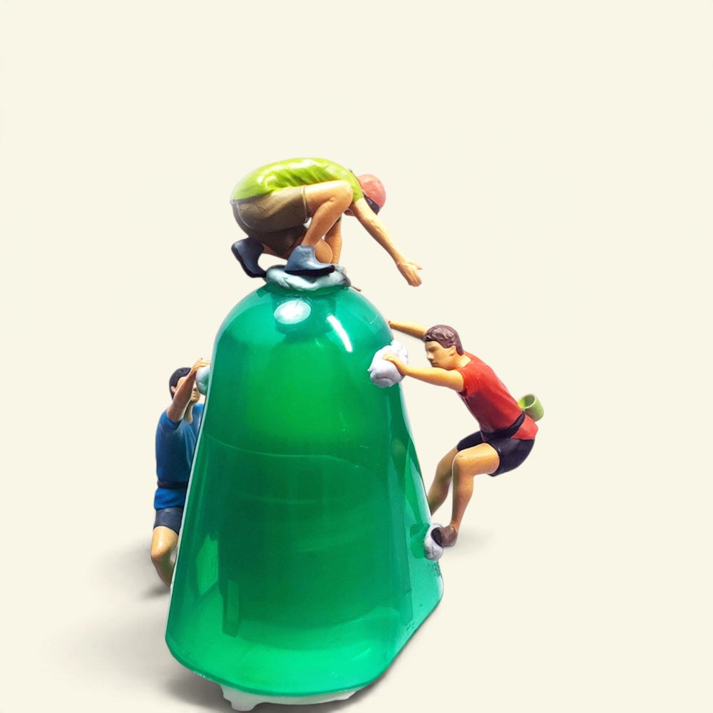 three 1:64 rock climbers seen from above on a green prop wall, the green one crouched on top, the red one gripping the side, the blue one below