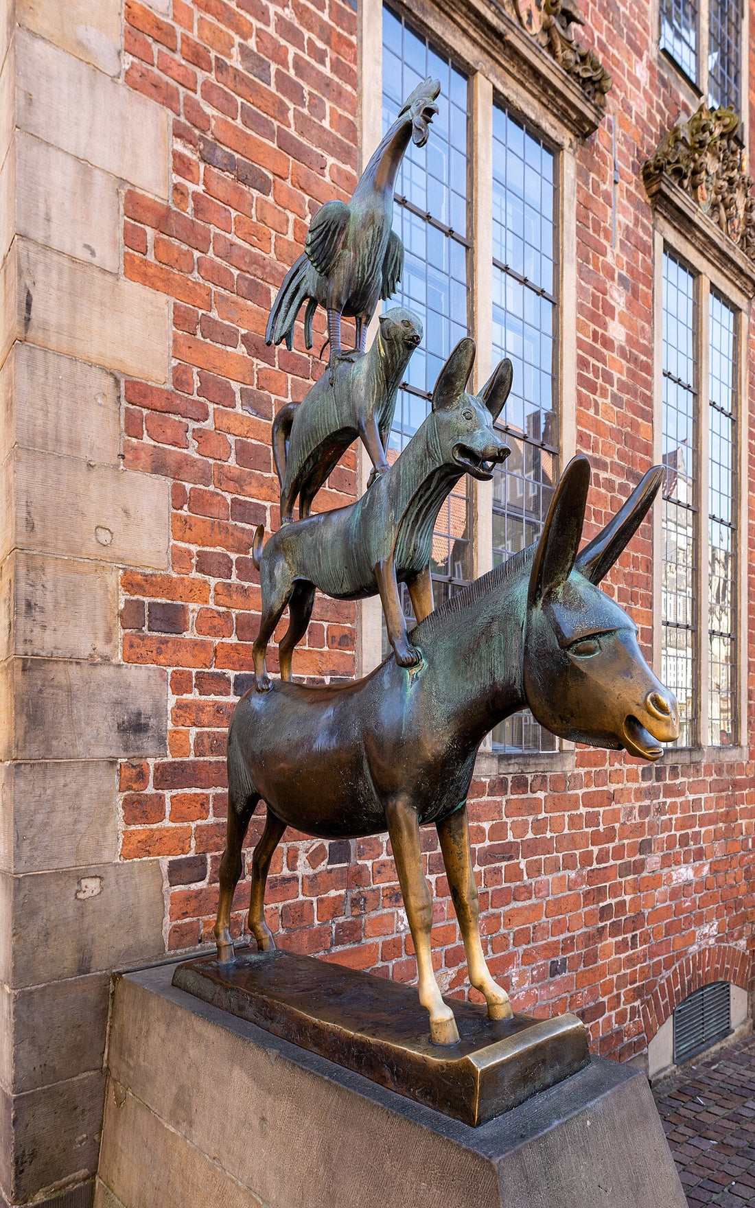bronze statue of the bremen town musicians next to bremen town hall: a donkey with a dog, a cat and a rooster stacked on its back