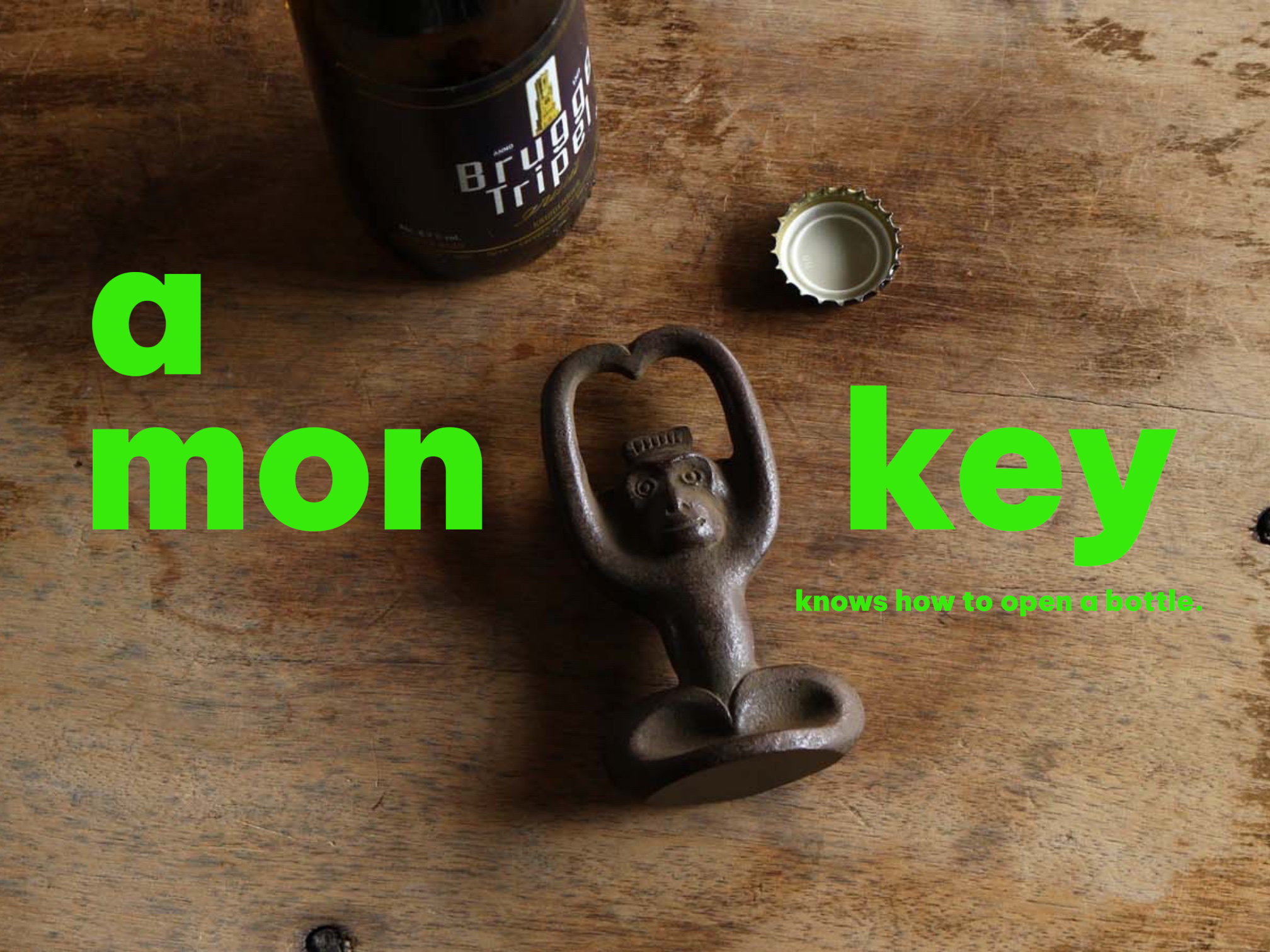 A cast iron monkey bottle opener lying arms-up on a weathered wooden table beside an opened beer bottle and its removed cap, with bright green text overlay reading 'a monkey knows how to open a bottle'.
