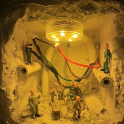 round led light glowing inside a wall hole while 1:87 workers stand among pipes and red and green wires