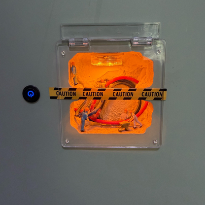 the finished piece on a grey wall next to a light switch: a small glowing job site under a clear hinged cover