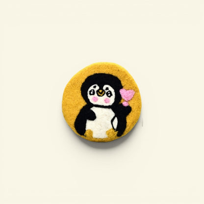 handmade wool felt penguin coaster, yellow colorway — embroidered penguin holding a heart, made in nepal