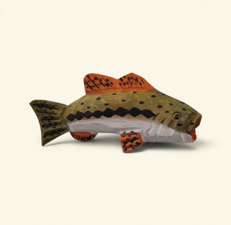 A handcrafted wooden fish figurine shaped like a trout, featuring a brown and green wood-grain body with orange and black spotted fins, set against a solid off-white background. uggaz