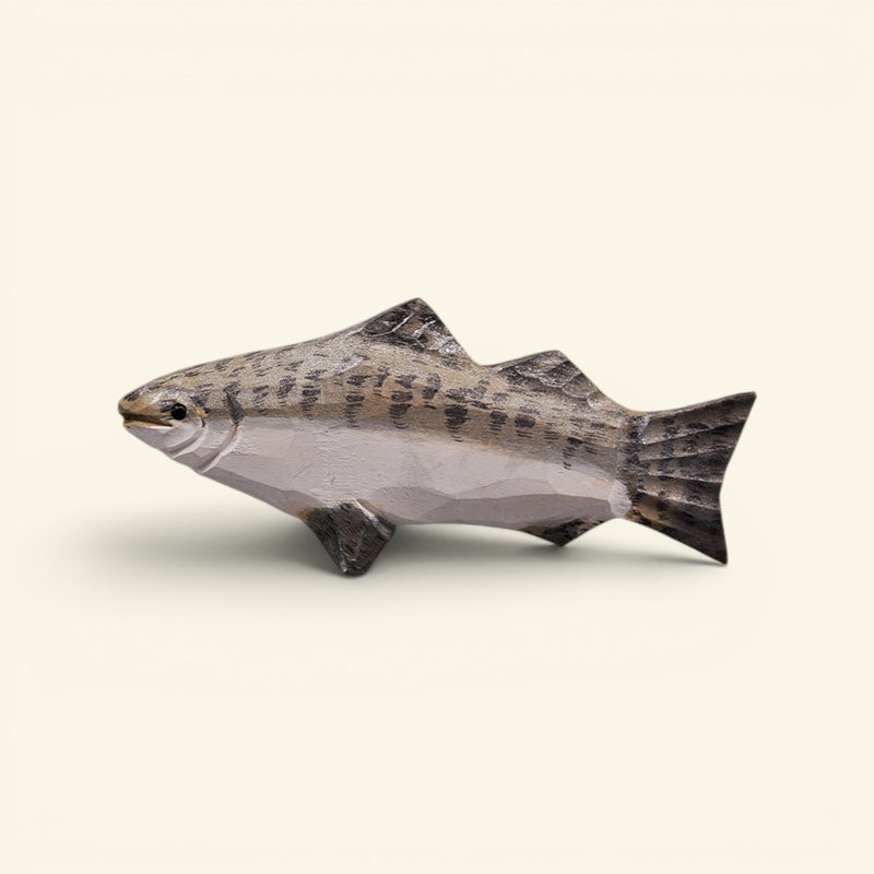 A realistic fish figurine or sculpture with a speckled gray and black pattern on top and a smooth light gray underside, shown against a plain light beige background. uggaz