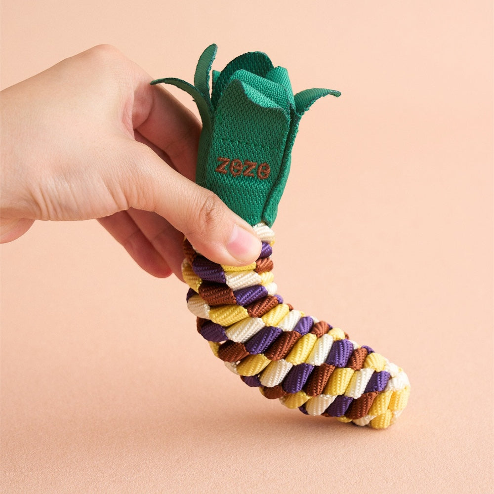 Hand holding The Knot Harvest corn rope toy, showing the husk-leaf detail