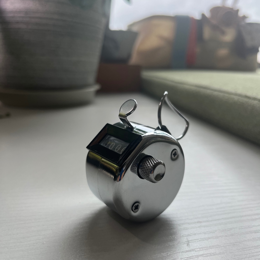 the tally counter – metal, resting on a windowsill mid-count, uggaz