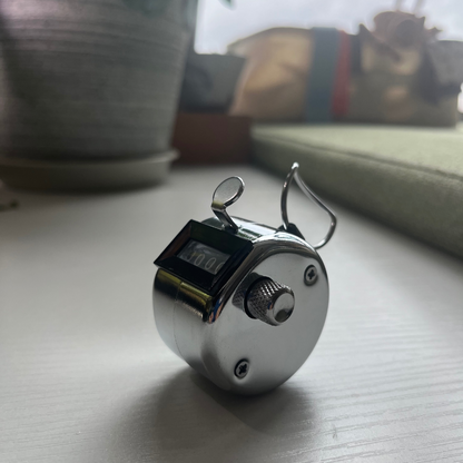 the tally counter – metal, resting on a windowsill mid-count, uggaz