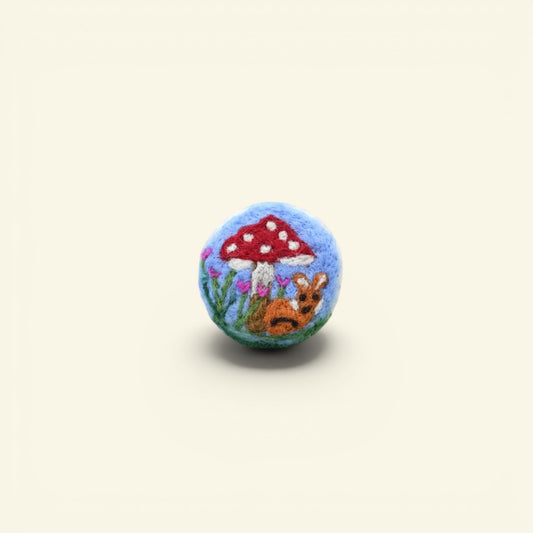 handmade wool felt brooch — bunny resting under a red and white mushroom on blue, needle-felted in nepal