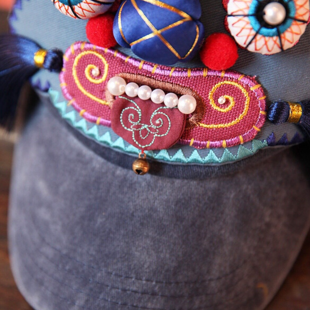 close-up of the tiger head cap's mouth — pearl-bead teeth, swirled embroidery, and the small brass bell underneath, uggaz