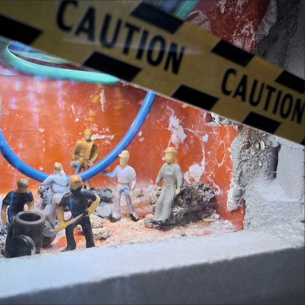 close-up of tiny workers at a red-walled switch box, blue wires overhead and caution tape in the foreground