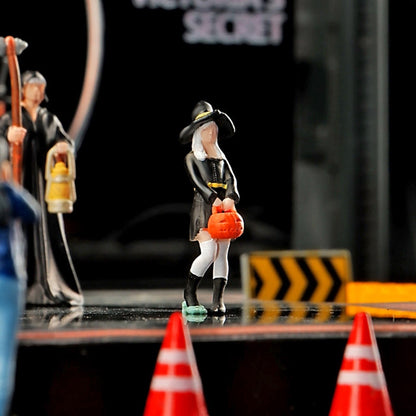 the 1:64 little witch standing between tiny orange traffic cones and a yellow chevron sign, the reaper beside her on a dark miniature street