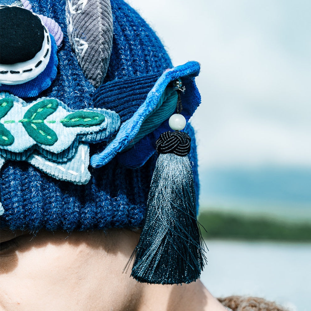 close-up of the ox head beanie's ear and beaded tassel in blue, lake in the background, uggaz