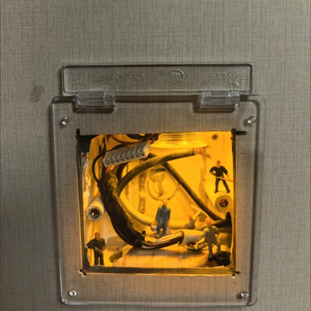 clear acrylic cover open on its hinge over a lit switch box full of cables and tiny workers