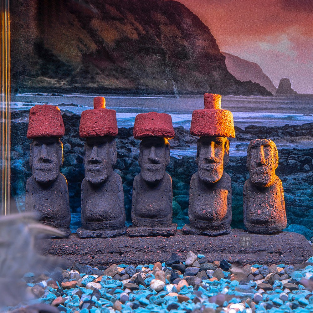 a hand placing a moai figurine into an aquarium, uggaz