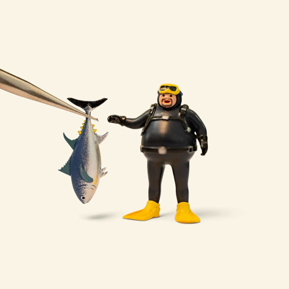 the diver, a 1:64 hand-painted resin figure, reaching for a separate tuna held in tweezers — the fish is its own piece