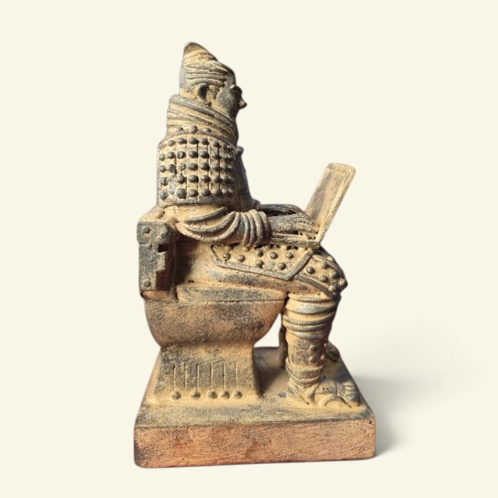 side profile of the toilet terracotta warrior figurine: seated on a carved toilet with the tank behind him, laptop open on his lap, on a square base, cream background