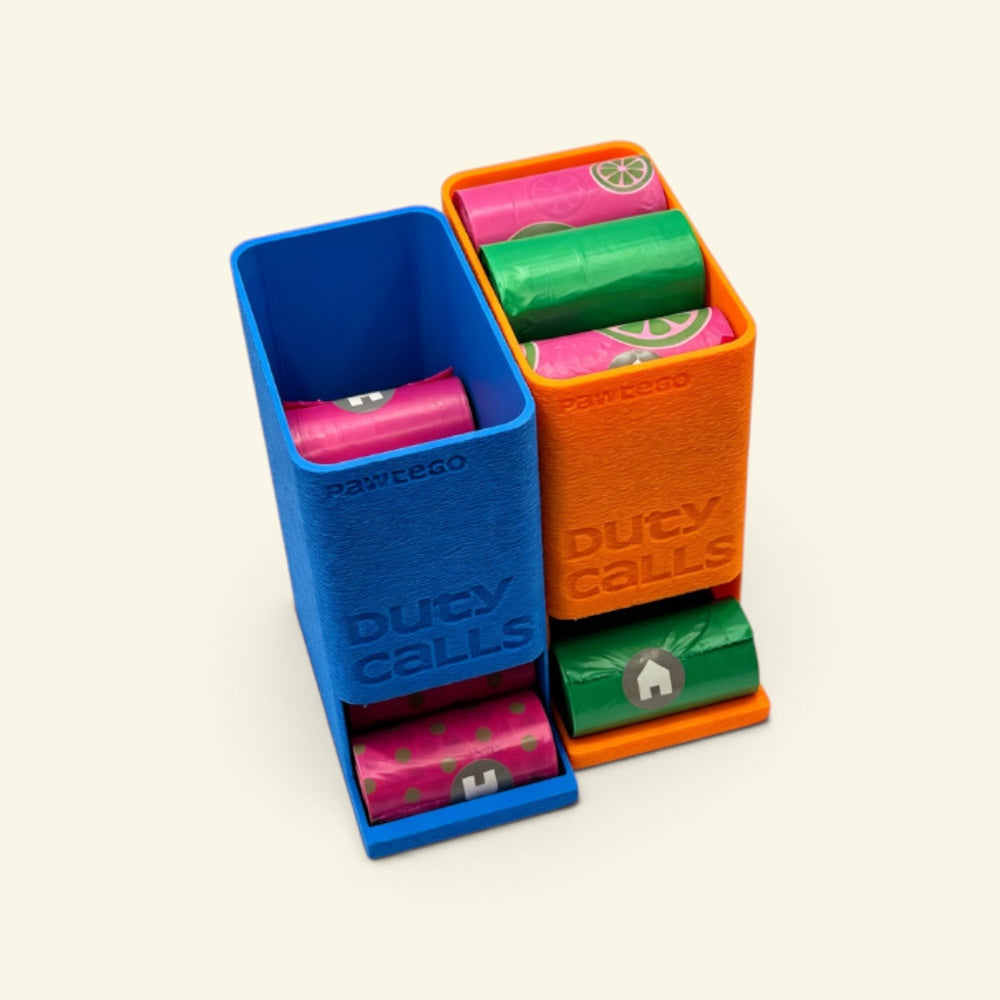 blue box open with no lid next to an orange box with its lid on, both embossed Duty Calls, a pink roll and a green roll dispensing from the bottom slots