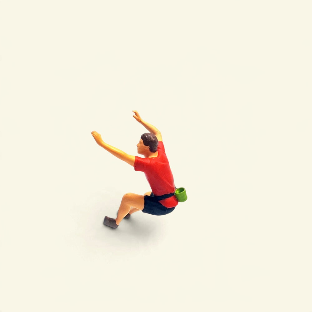 the red climber: a 1:64 hand-painted figure in a red t-shirt and black shorts with a green chalk bag, both arms up, leaning back mid-move
