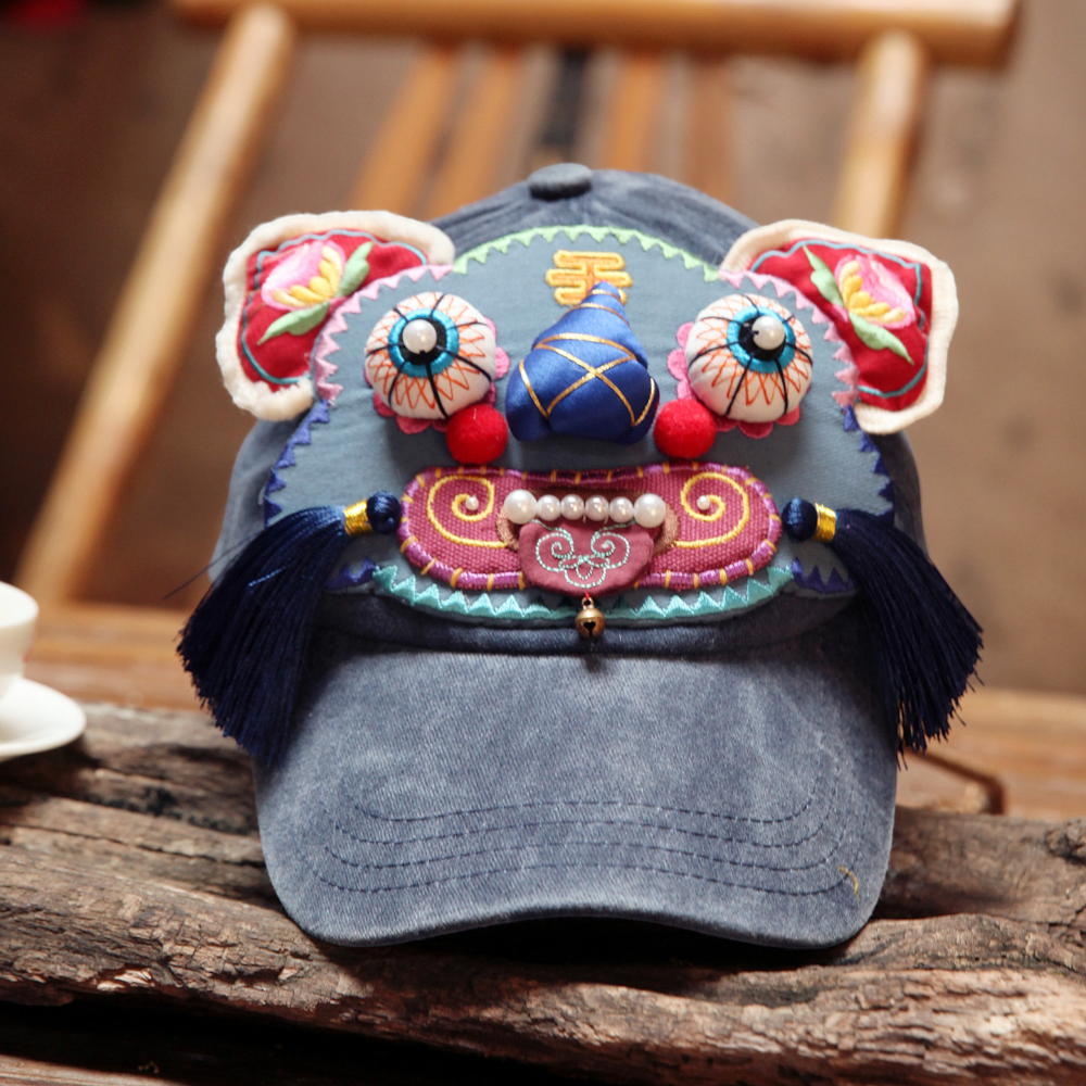 the tiger head cap resting on a wooden chair, full tiger face visible with pearl teeth and dangling tassels, uggaz