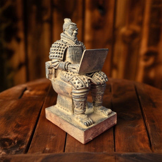 terracotta warrior on a toilet with a laptop, standing on a rustic wooden table in warm light, topknot, scale armor and square base visible