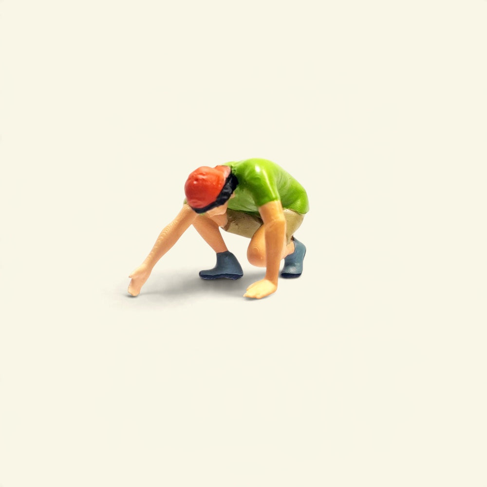 the green climber: a 1:64 hand-painted figure in a green t-shirt, khaki shorts and a red cap, crouched low with one hand reaching forward