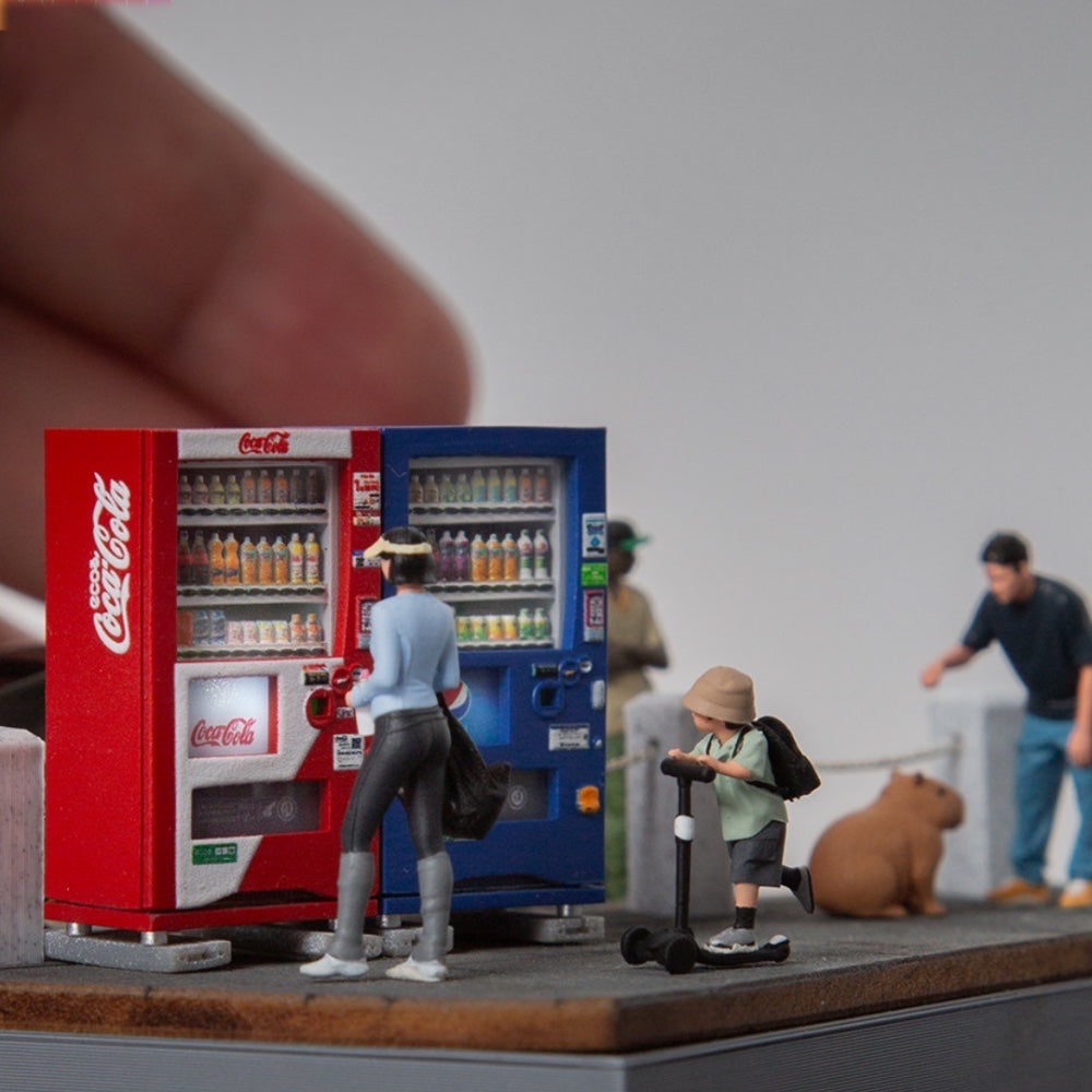 red and blue 1:64 vending machines side by side at eye level, a tiny figure buying a drink and a kid on a scooter nearby; figures and scene not included