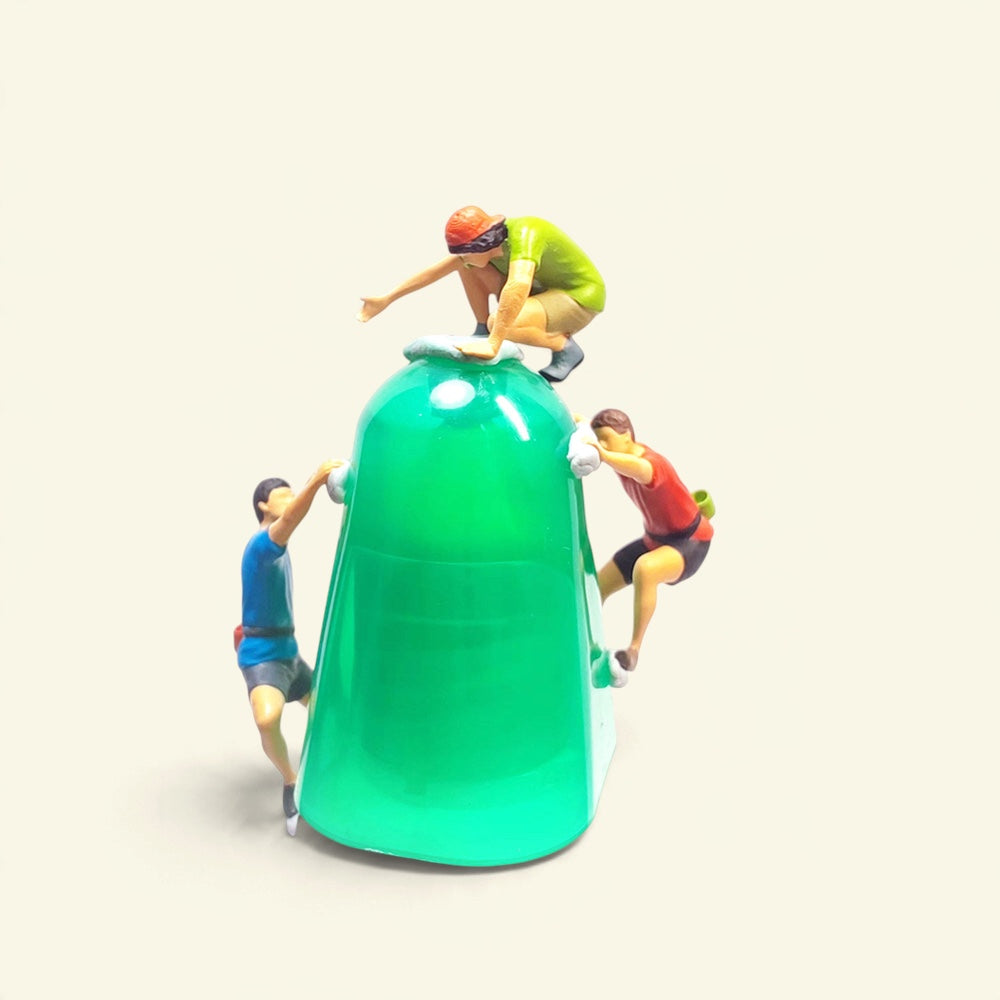 all three 1:64 rock climbers around a green prop wall: green shirt crouched on top, blue on the left, red on the right
