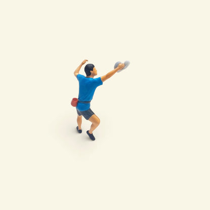 the blue climber: a 1:64 hand-painted figure in a blue t-shirt and grey shorts reaching up open-handed, red chalk bag at his hip (the grey hold is a photo prop)