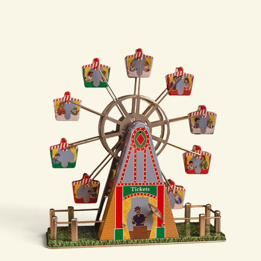 wind-up tin ferris wheel music box on a plain cream background — striped tin gondolas on thin wire spokes, a printed ticket booth tower and a little fence around the grassy base