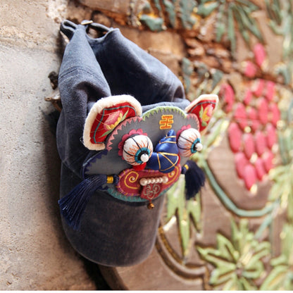 the tiger head cap hanging against a stone wall with pink flowers in the background, tiger face and tassels in profile, uggaz