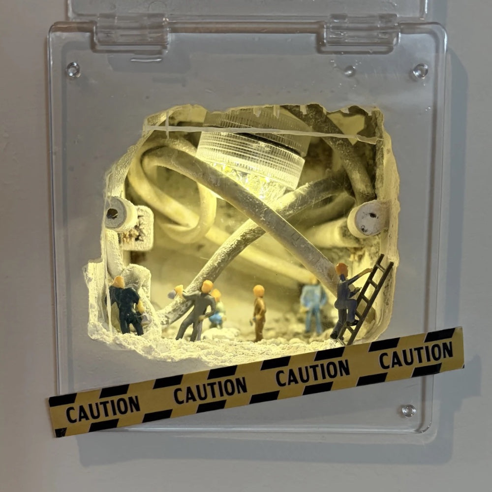 clear hinged cover over a lit wall hole, tiny workers and a ladder among cables, caution tape angled across the front