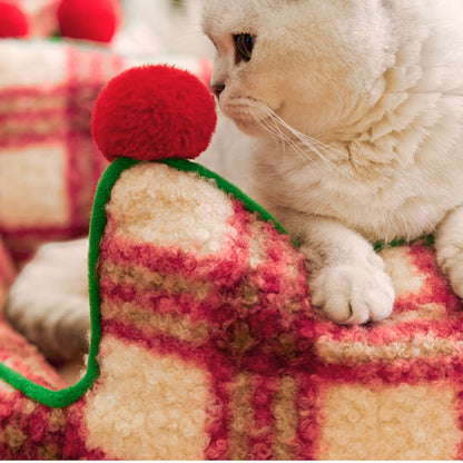 close-up of a white cat beside a red pom-pom on the plush plaid wall of the plaid throne