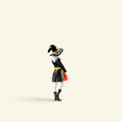 the 1:64 little witch from the side, pointed black hat and pumpkin bucket, on a cream background