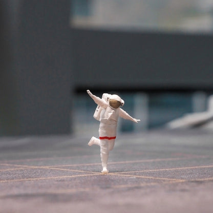 the happy astronaut 1:64 figurine dancing on one foot across a grey miniature pavement, city blurred behind him