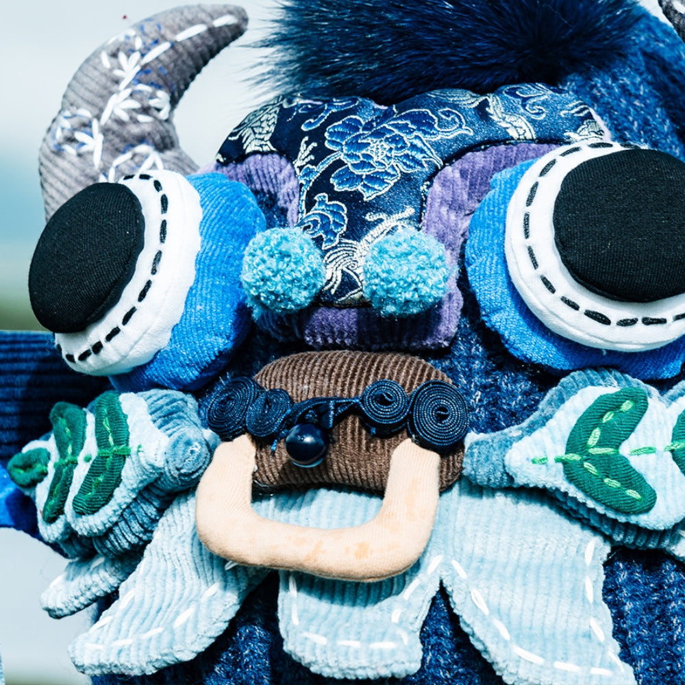close-up of the ox head beanie's face in blue — horns, bead eyes, pompoms, and wooden toggle nose, uggaz