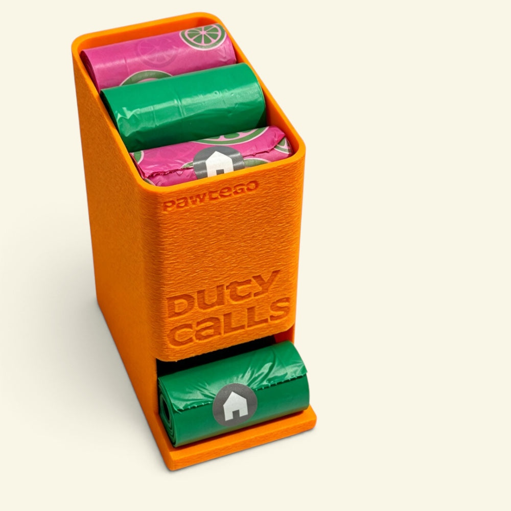 orange Duty Calls box loaded with citrus-print pink and solid green bag rolls, one green roll dispensing from the bottom slot