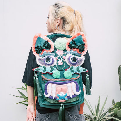 the tiger pack worn on someone's back against a plain background, tiger face and dangling tassels visible from behind, uggaz