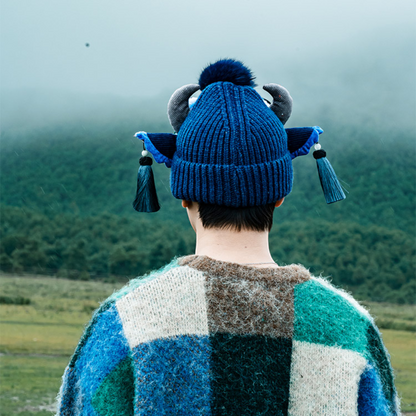the ox head beanie in blue from behind, showing the horns and tassels over a forest landscape, uggaz