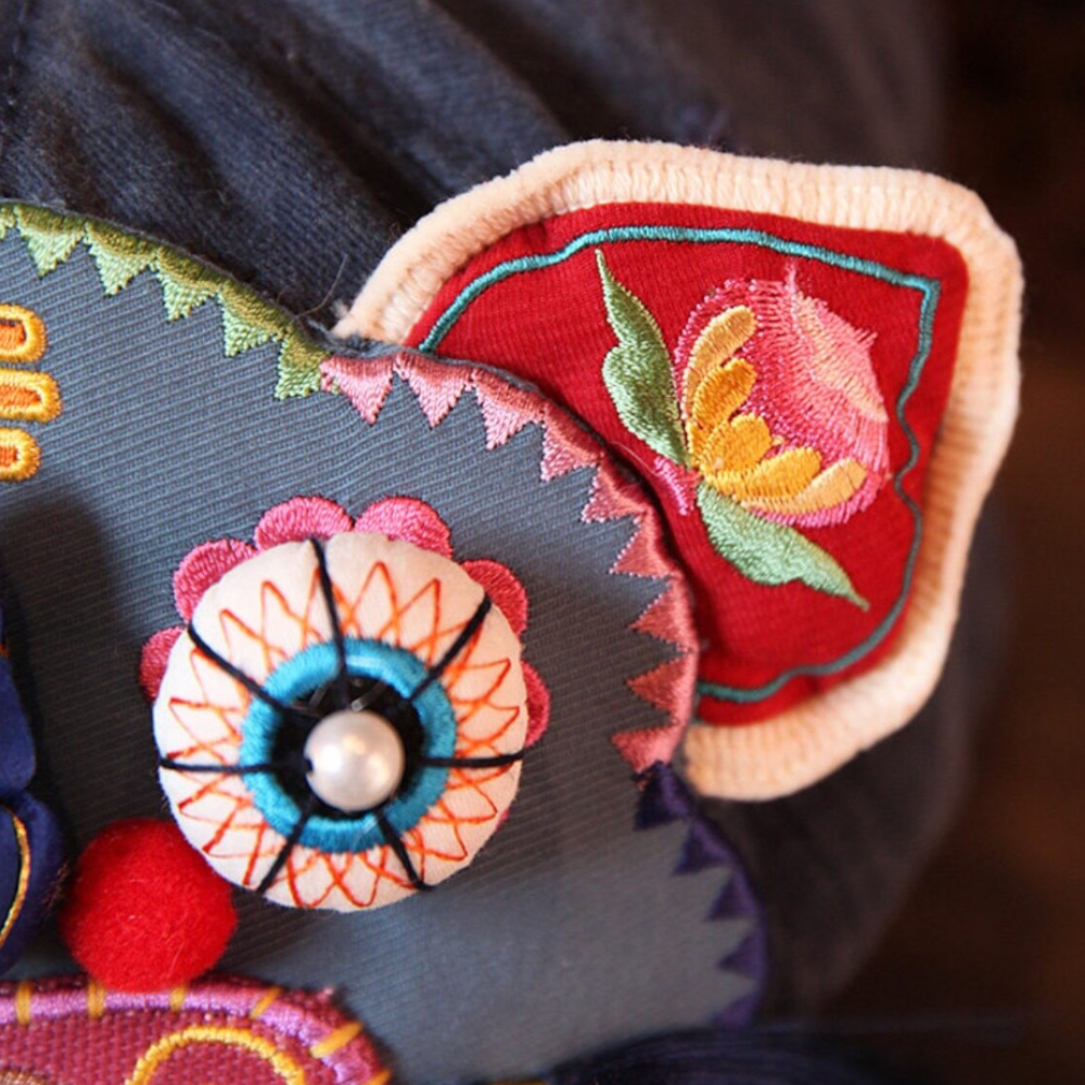 close-up of the tiger head cap's embroidered ear and one bead eye, pearl center and floral detail, uggaz