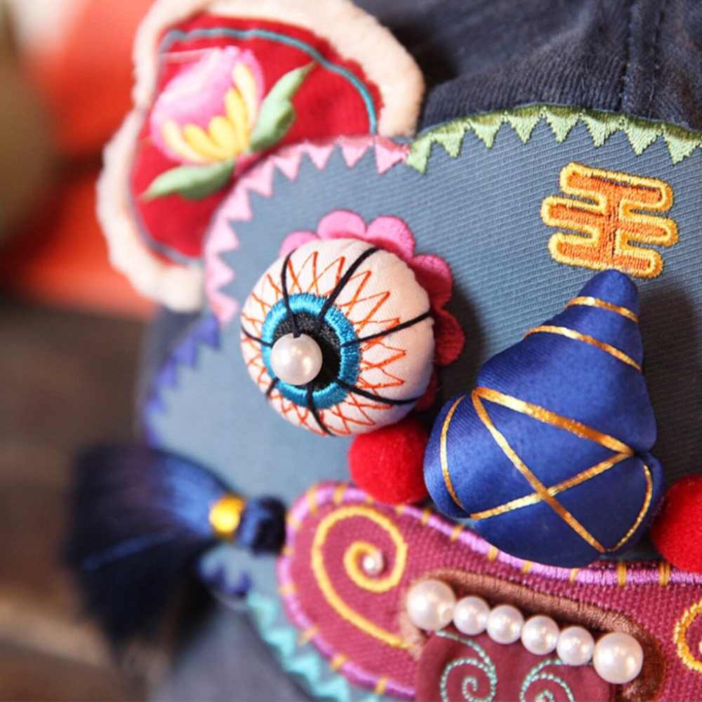 close-up of the tiger head cap's twisted blue nose, bead eye, and gold embroidered charm, uggaz