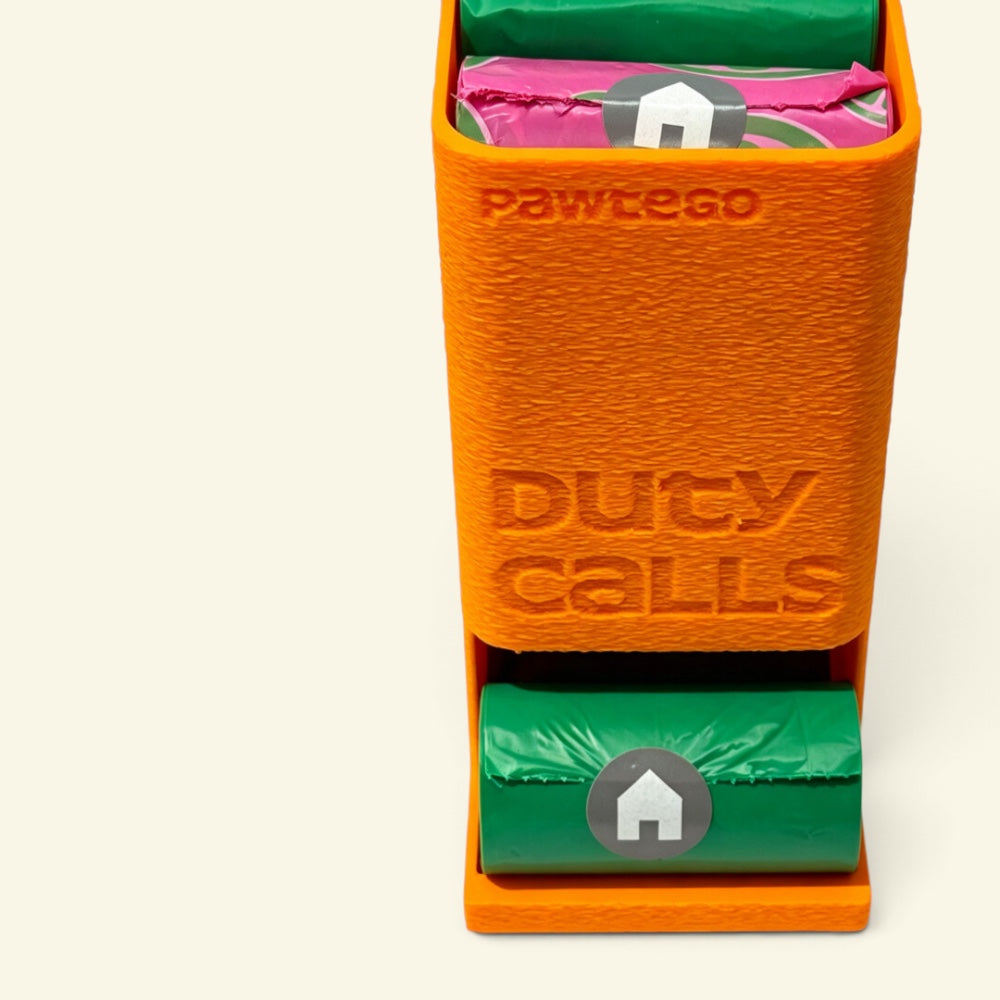 close-up of the orange Duty Calls box with its lid on, showing the embossed Pawtego Duty Calls text and 3D-print texture, green and pink rolls loaded inside
