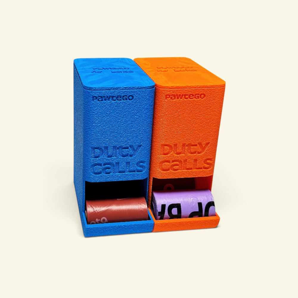 blue and orange Duty Calls boxes side by side with their lids on, dispensing a brown roll and a lavender roll from the front slots