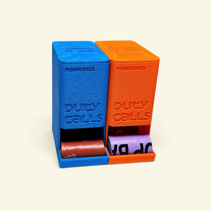 blue and orange Duty Calls boxes side by side with their lids on, dispensing a brown roll and a lavender roll from the front slots