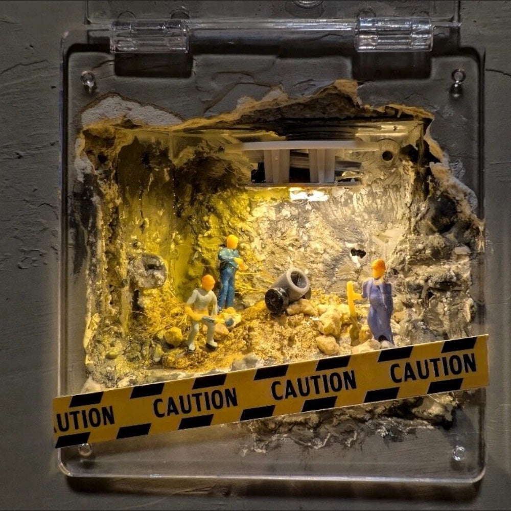 hole in a wall turned into a tiny dig site under a hinged clear acrylic cover, 1:87 workers lit by a warm yellow light, caution tape across the front