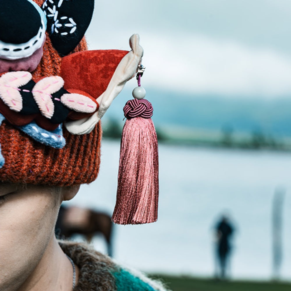 close-up of the ox head beanie's tassel in dusty rose, lake and a horse blurred in the background, uggaz