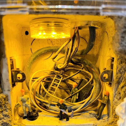 coiled wires inside a switch box, a worker on a ladder and others on the floor under a yellow led light