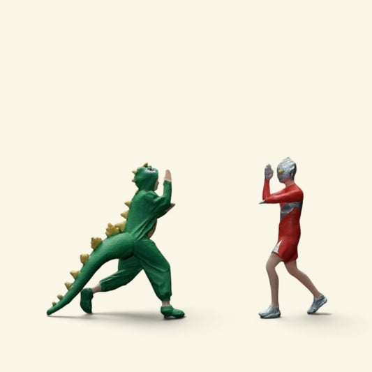 two 1:64 scale hand-painted figures on a cream background: a person in a green dinosaur onesie with yellow spikes squaring off against a hero in a red-and-silver suit and gym shorts
